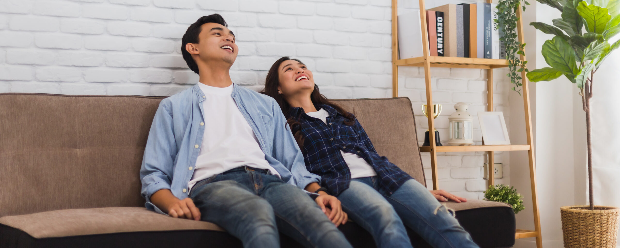 Young Asian couple lover sitting on sofa after moving it to new home background.