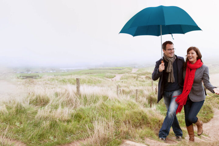 man and woman with red scarf under blue umbrella on beach