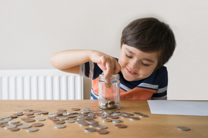 School Kid putting money coins into clear jar, Child counting his saving money, Young boy holding coin on his hands, Children learning about saving for future concept