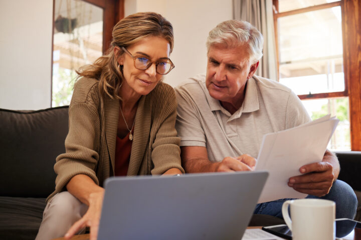 Retirement couple budget, finance and investment planning, loan and paper bills with laptop technology in home. Mature people money, cash savings or legal insurance document report on online bank.