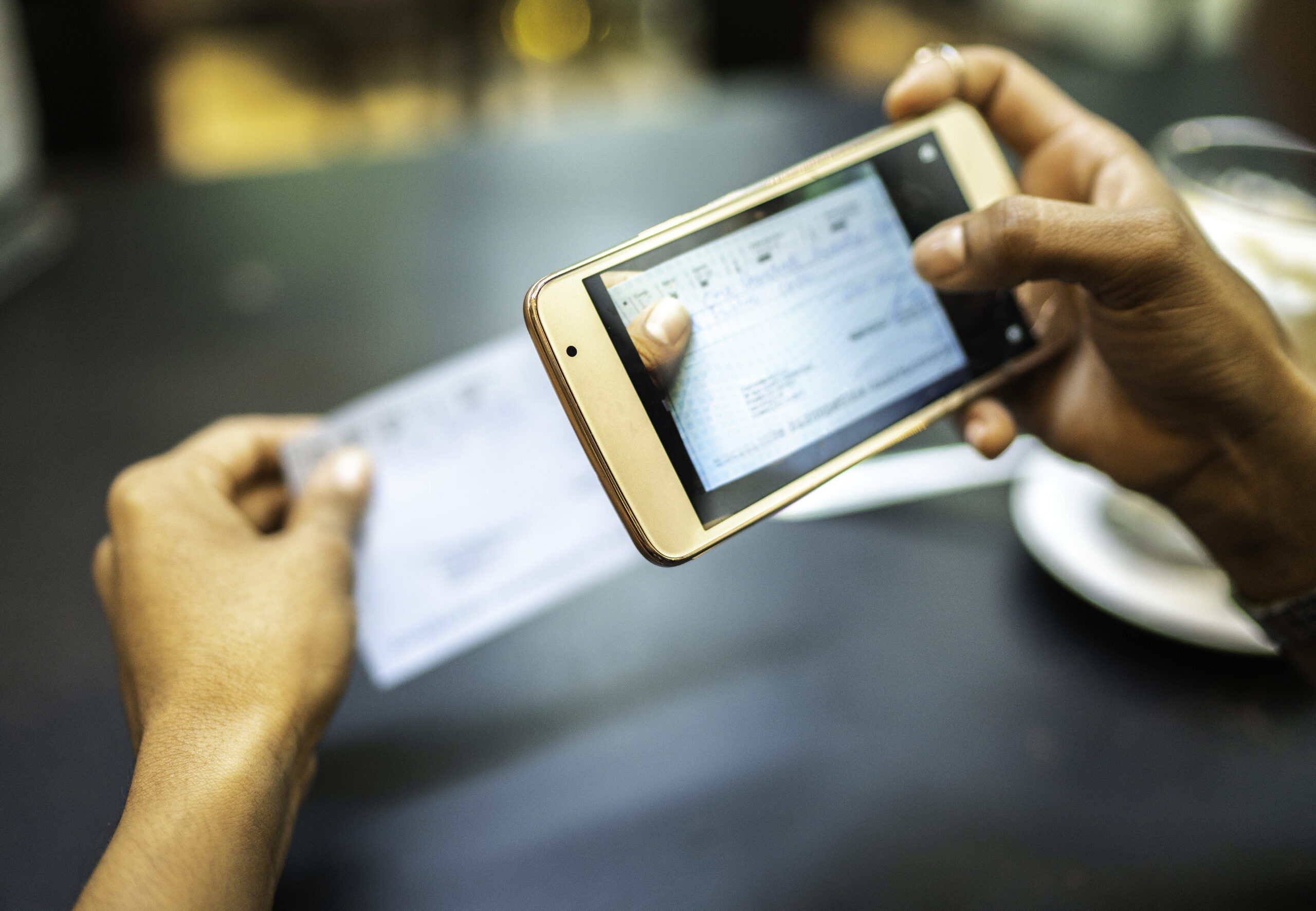 Young woman depositing check by phone in the cafe