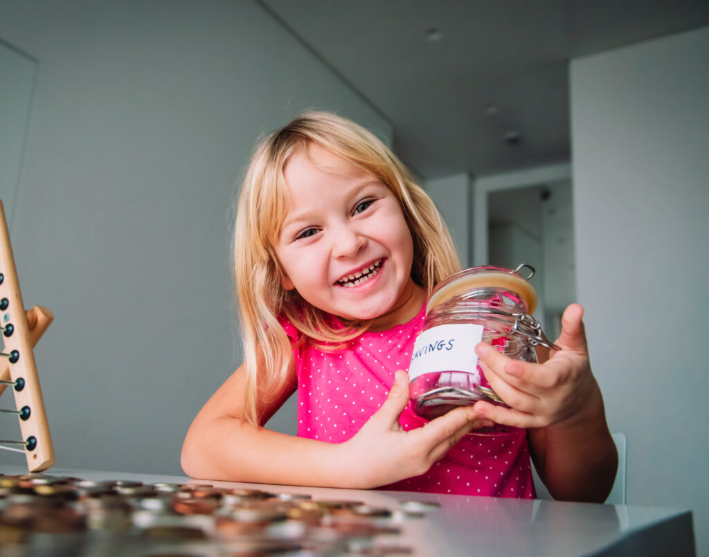 happy girl counting money, cute child put coins into saving jar
