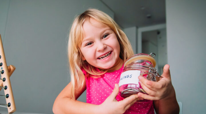 happy girl counting money, cute child put coins into saving jar