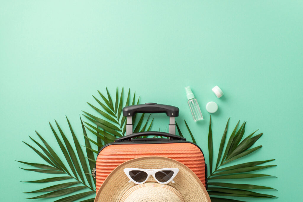 A captivating turquoise setting sets the stage for a top view of a suitcase, beach gear, sunglasses, headwear, spf cosmetic bottles on palm leaves. Great for travel marketing