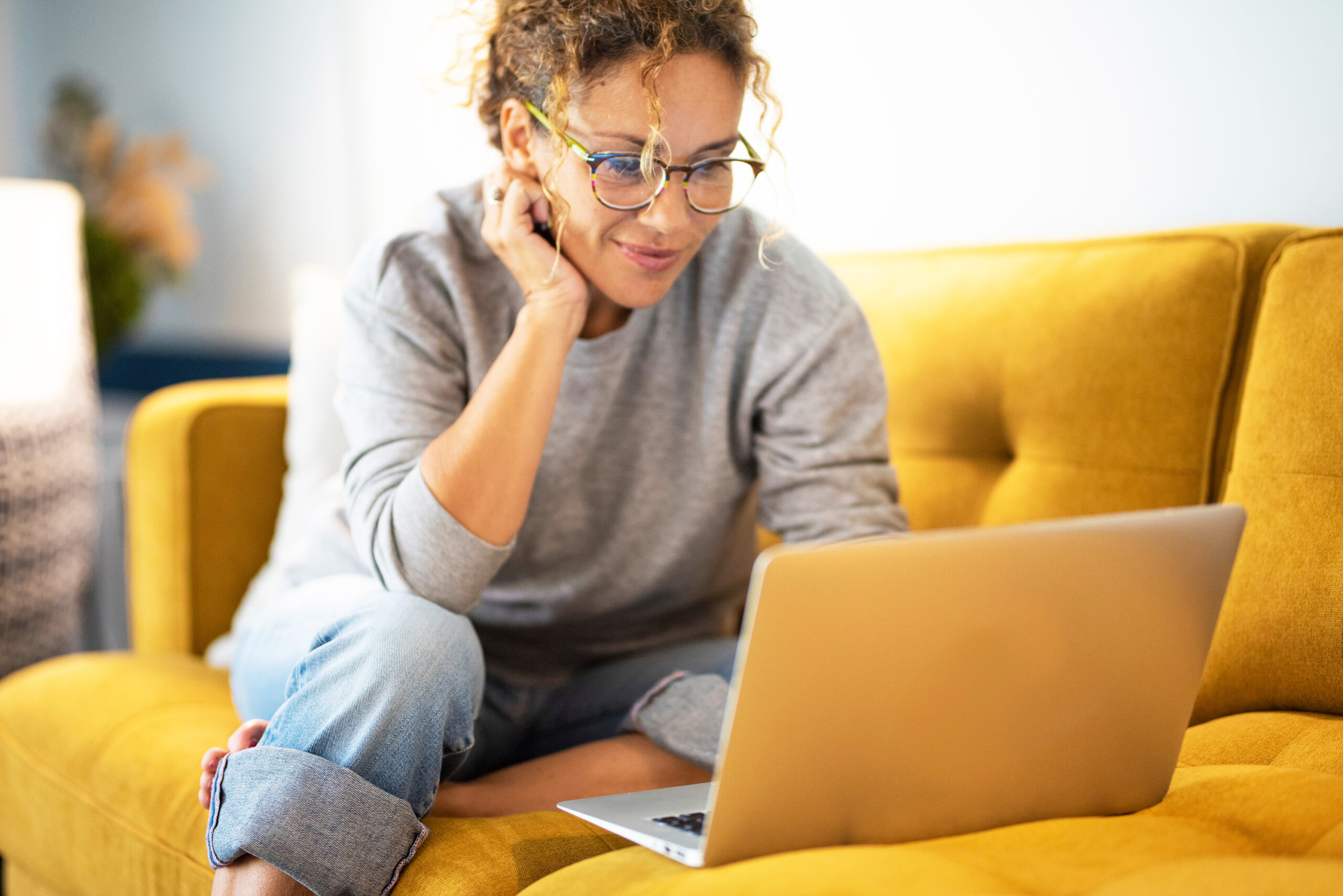 Female sitting on a yellow couch using laptop and internet connection and smile.